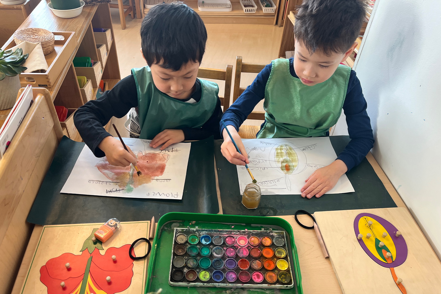 Two students using paint and paintbrushes to depict the flowers on their flower puzzles.