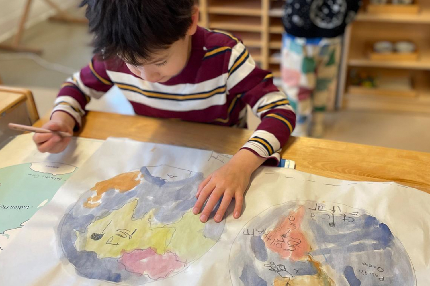 A student focused on his work, depicting earth's many continents and bodies of water with pen and paint.