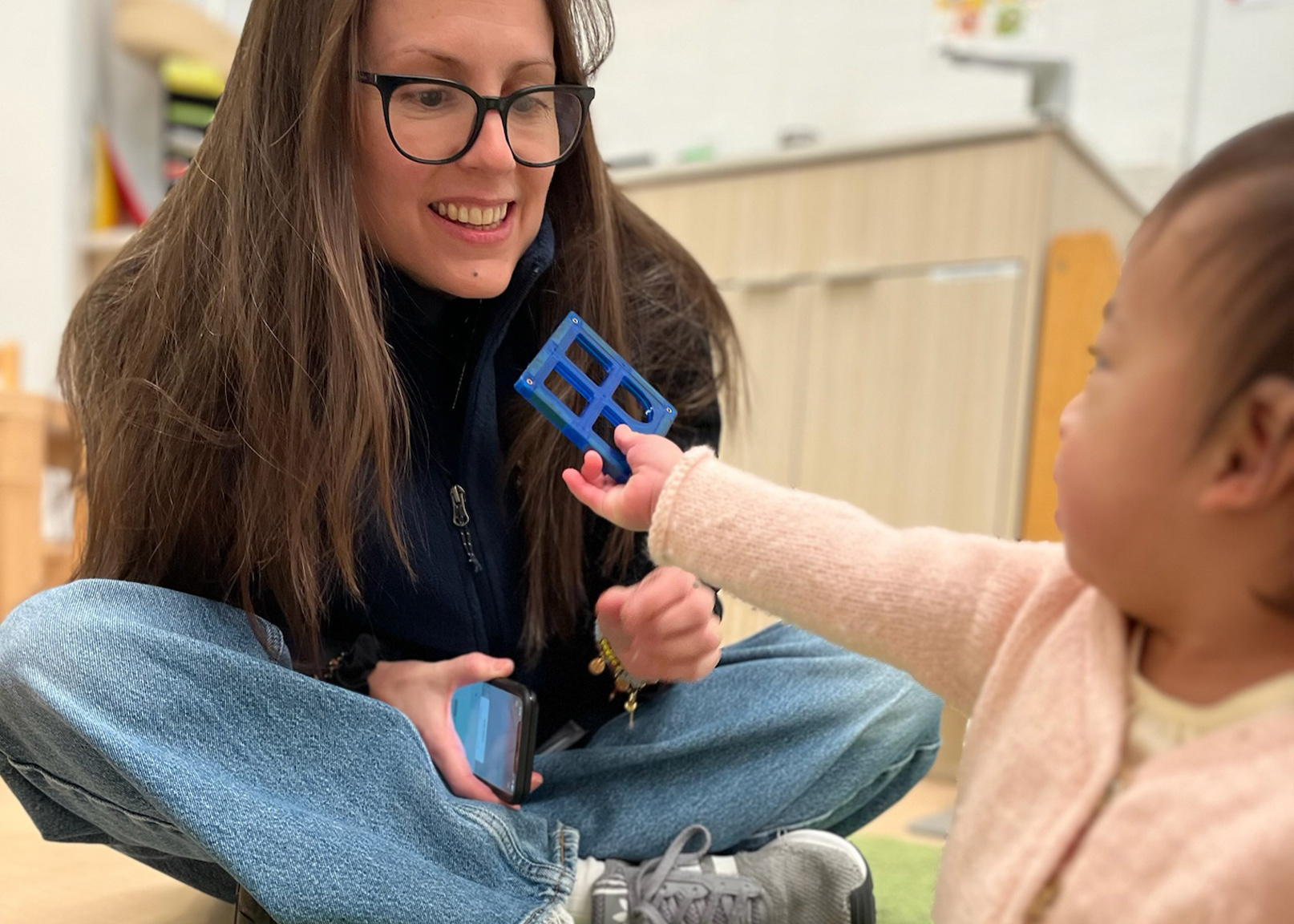 Battery Park Montessori teacher smiles as student hands her a magnet toy 