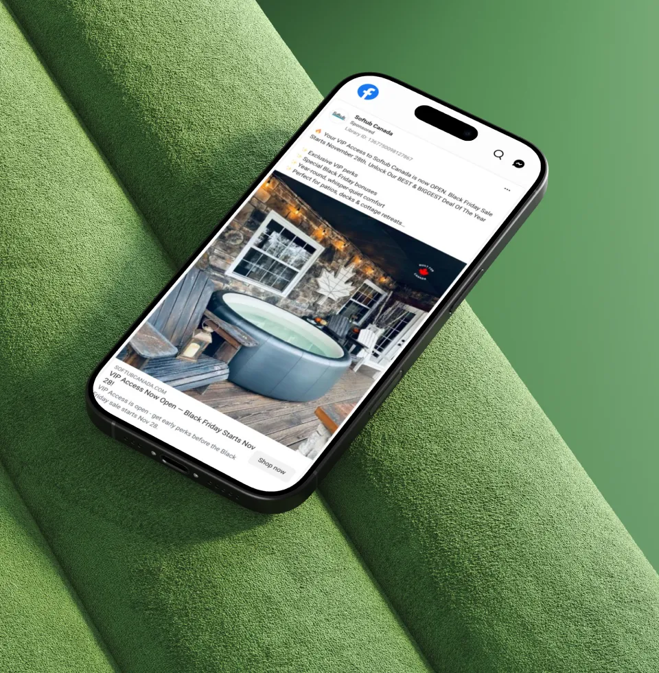 Smartphone on green textured surface displaying a Facebook advertisement from SofTub Canada promoting VIP access to a Black Friday sale, featuring an image of an outdoor hot tub on a wooden deck with stone wall background and outdoor furniture.