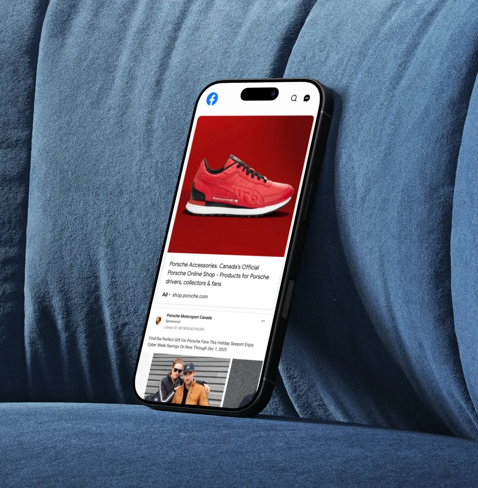 Smartphone displaying a Facebook ad for Porsche Accessories featuring a red sneaker on a red background, placed on a blue fabric surface.
