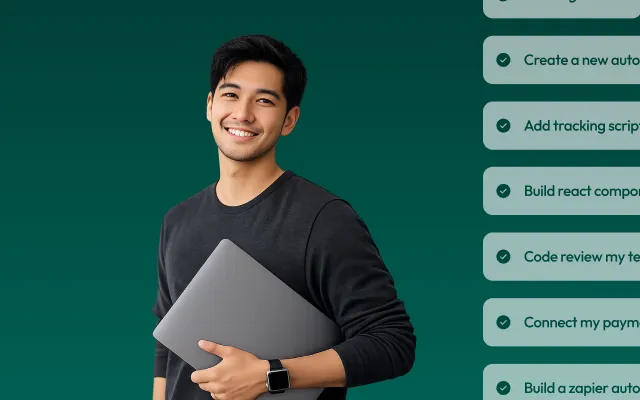 Smiling young man with black hair and a black long-sleeve shirt holding a closed gray laptop against a dark green background.