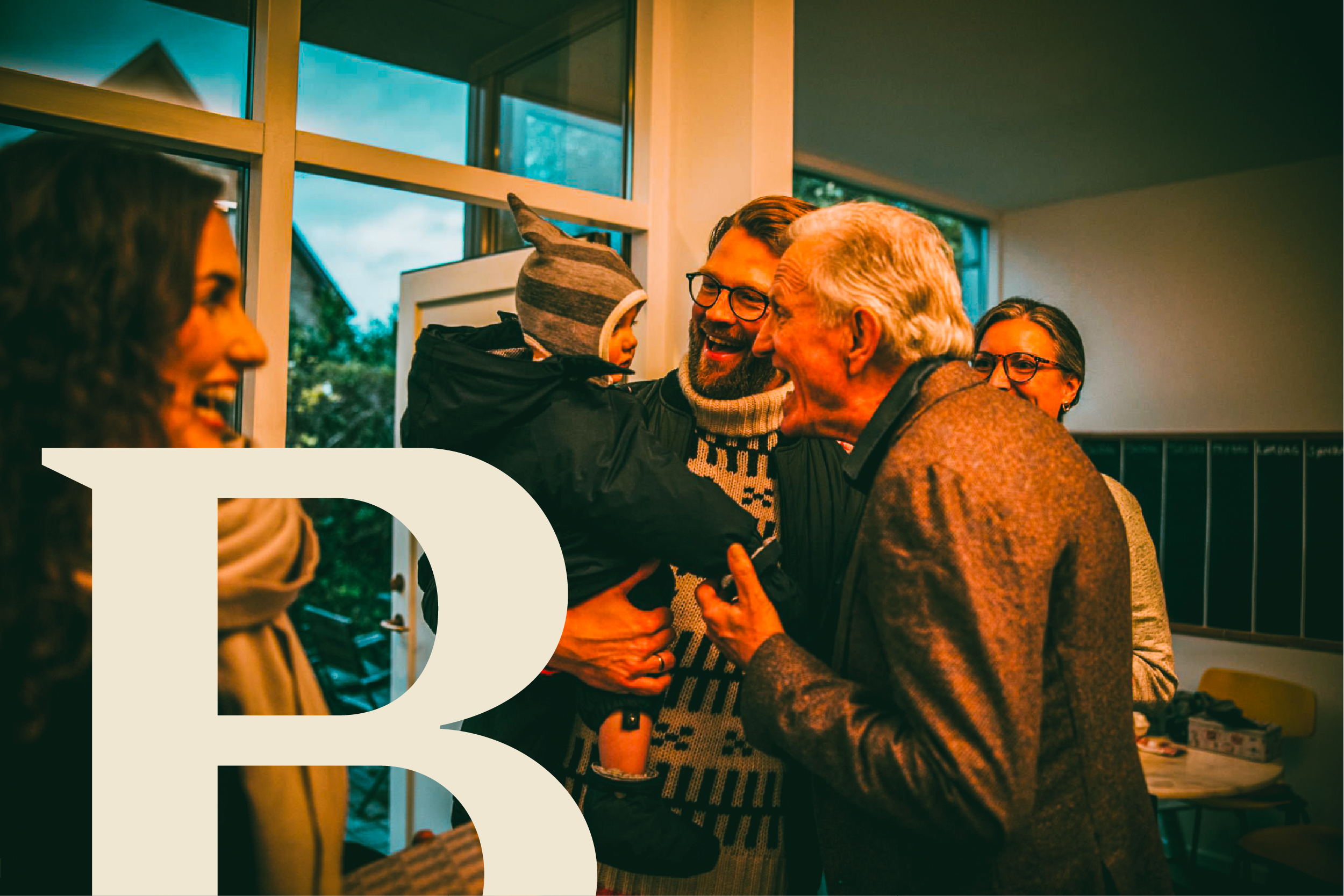 An older man embraces a man carrying a small child indoors.