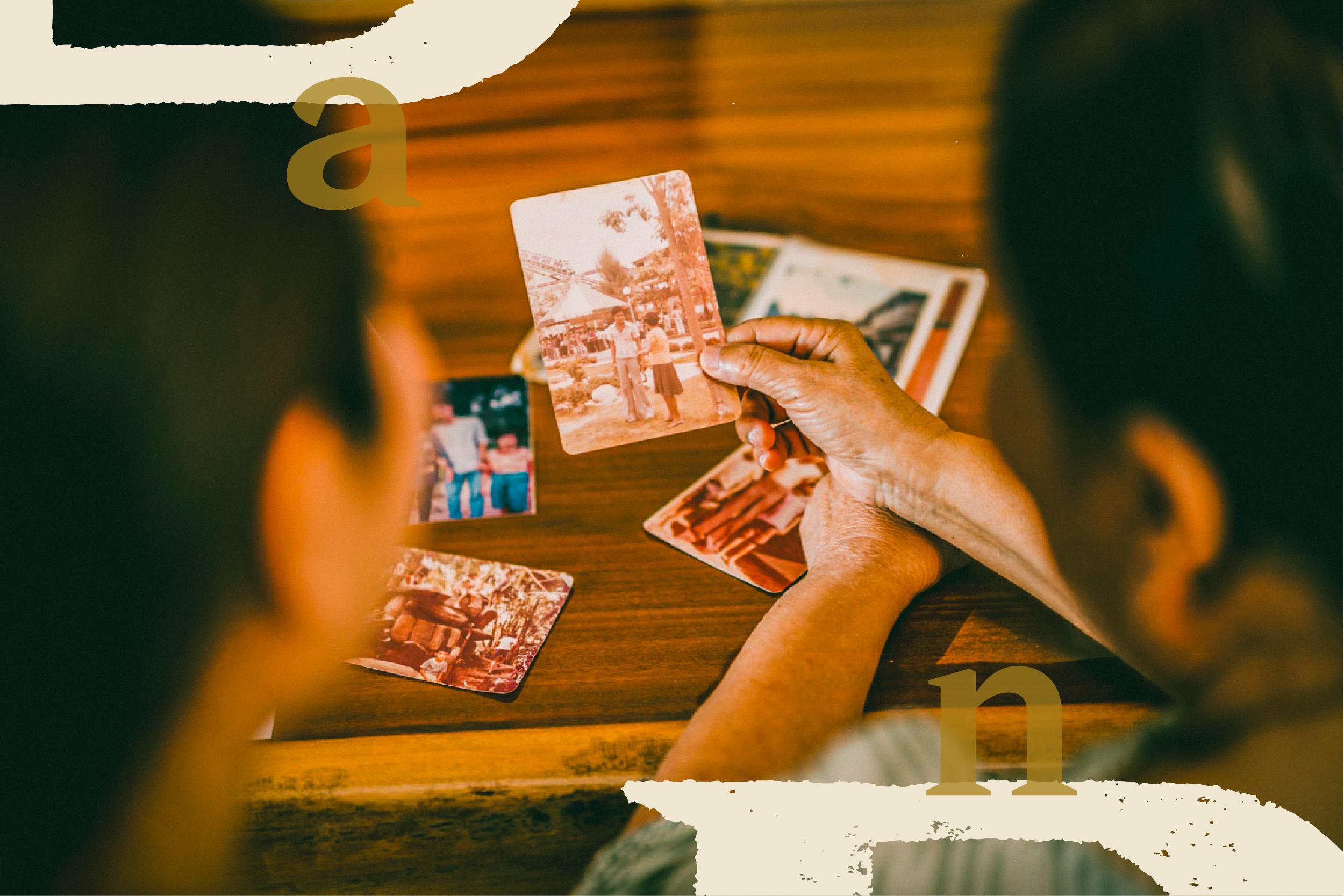 Hands hold a printed photograph above more photos on a wooden table.