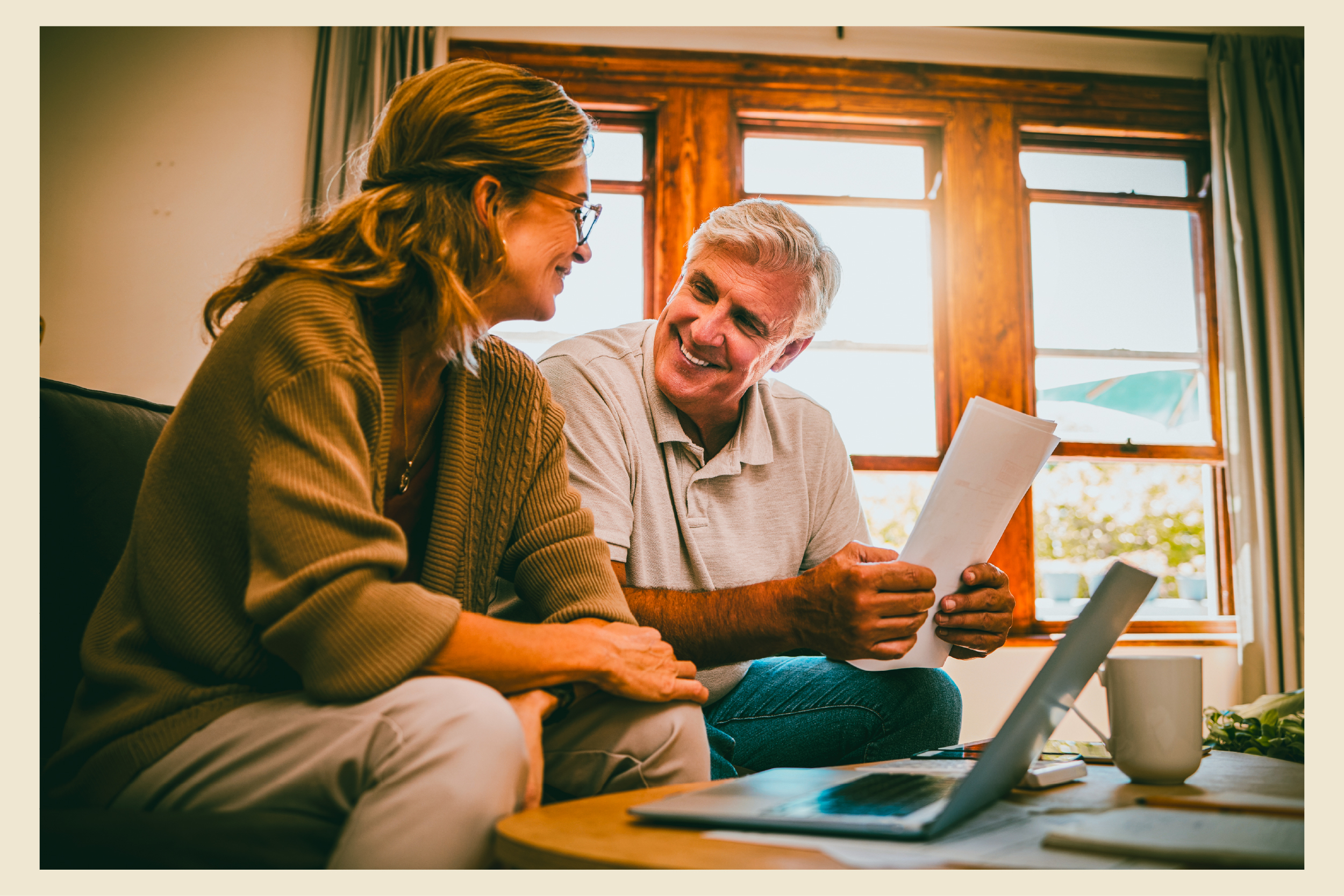 An older couple read a document together beside a laptop at home.