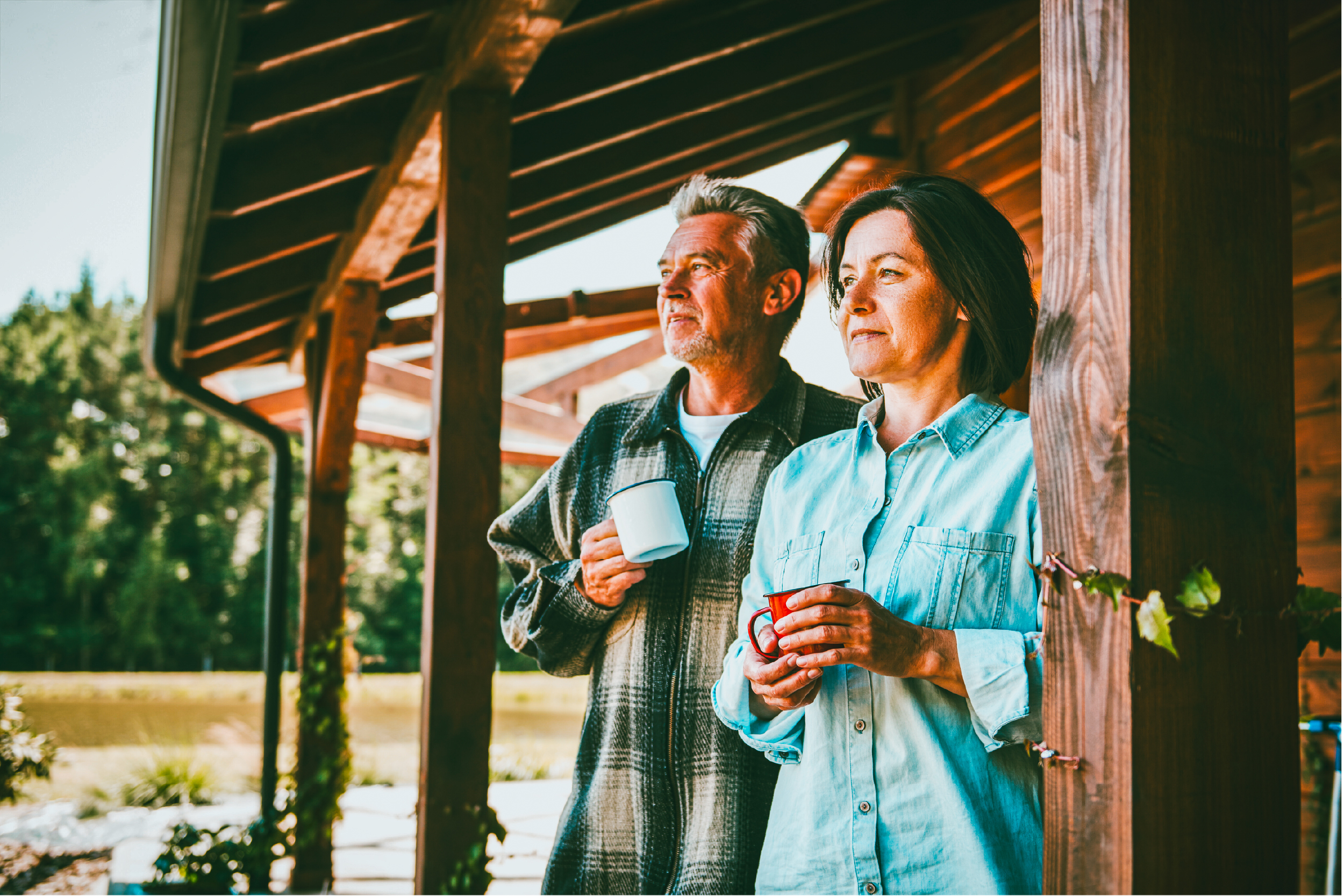 A couple hold mugs on a wooden porch and look into the distance.