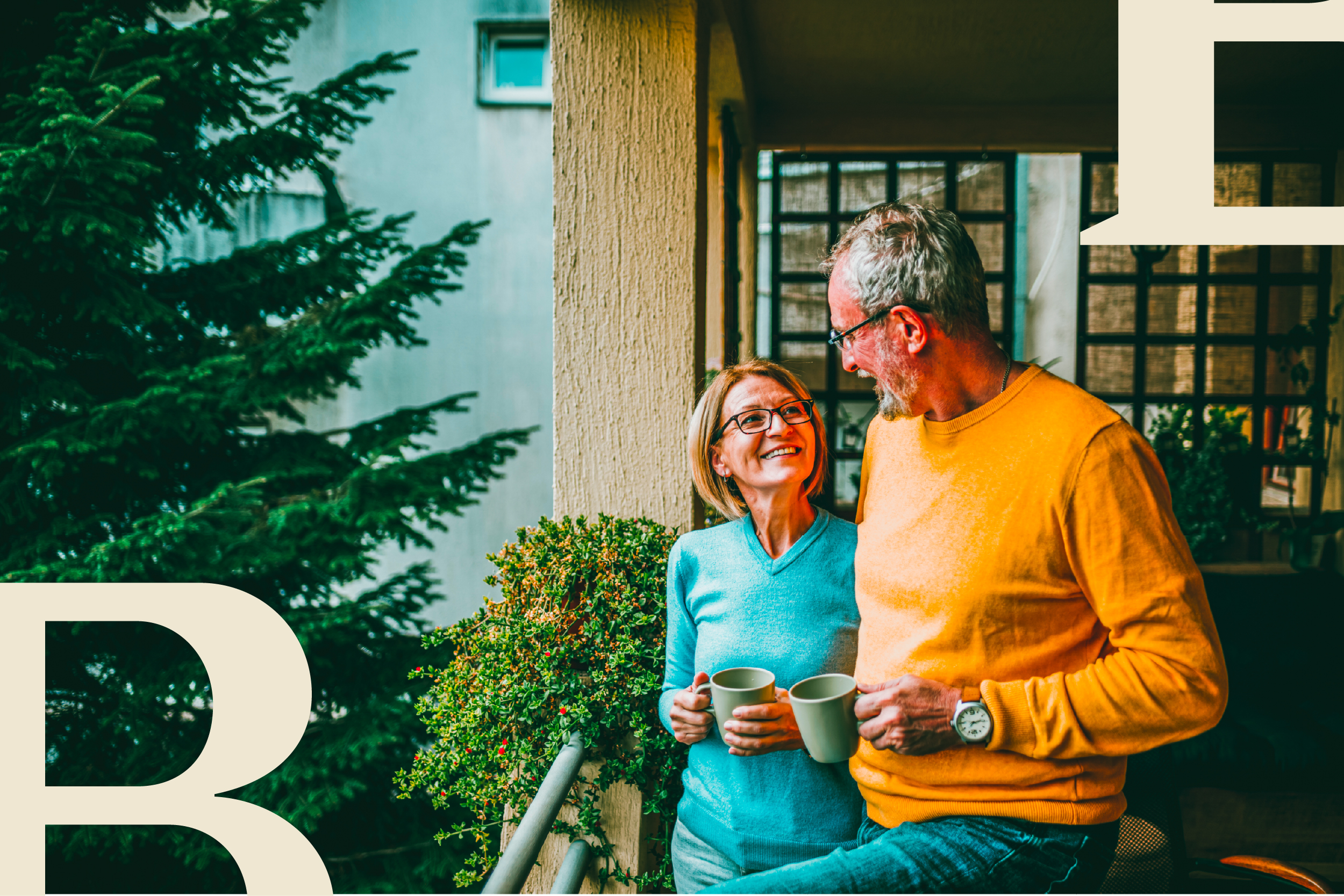 An older couple hold mugs and smile at each other on a balcony.