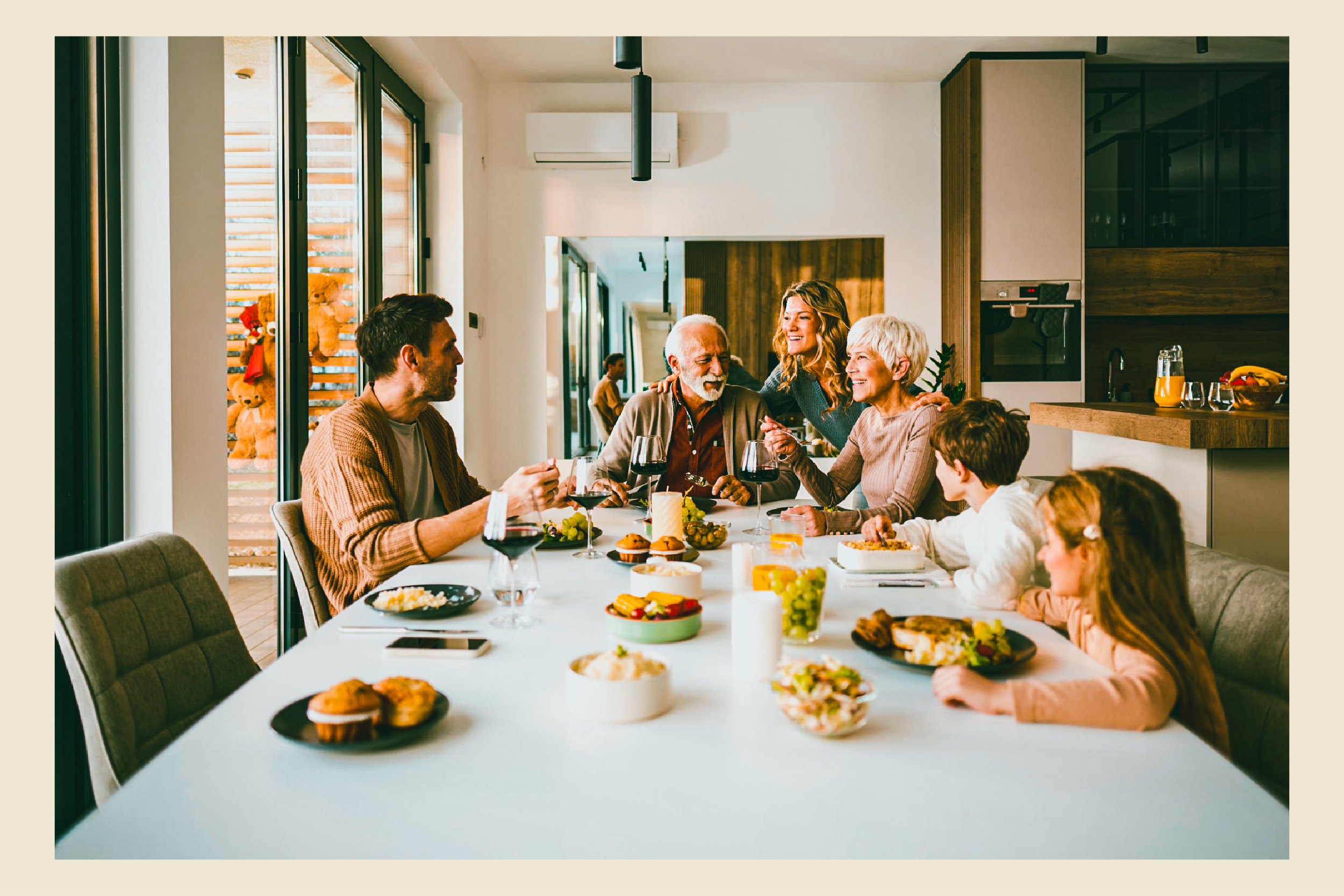 Three generations share a meal at a white table in a modern kitchen.