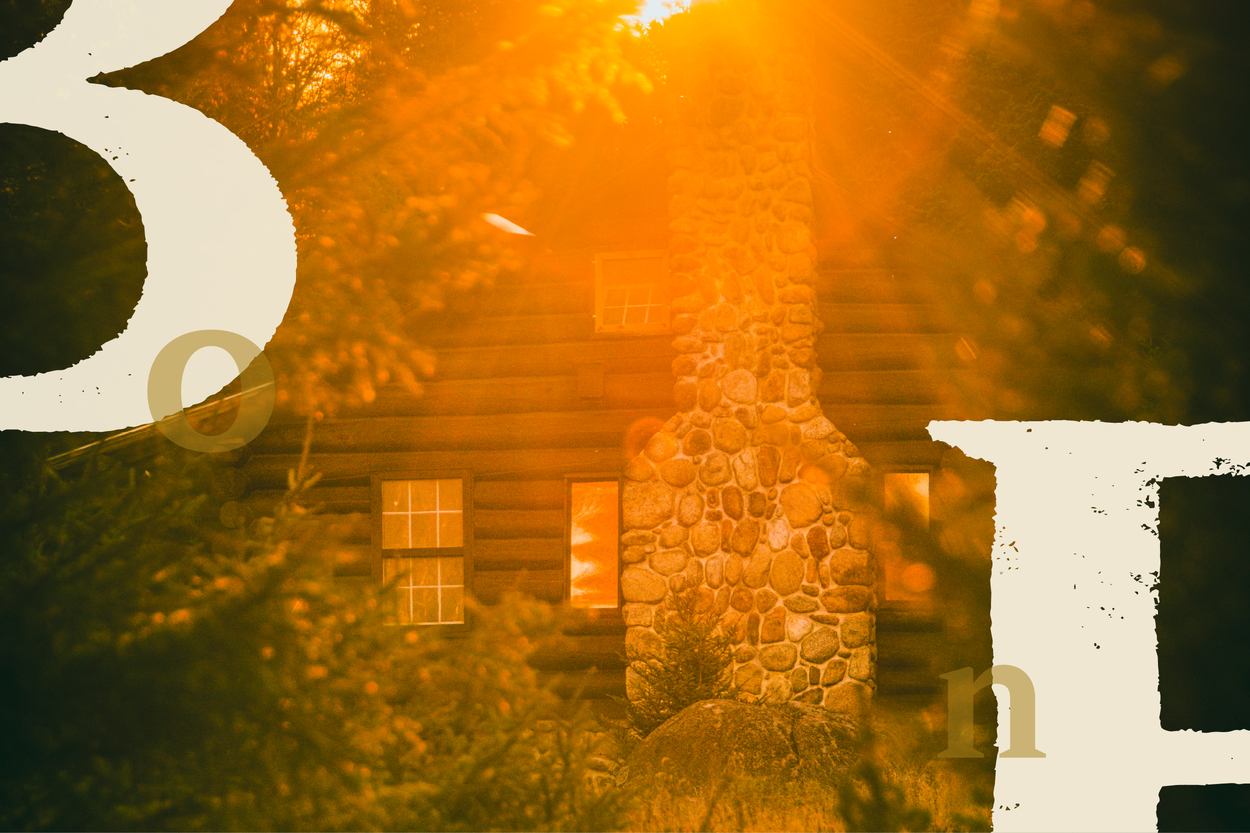 A log cabin with a stone chimney glows in sunlight through trees.