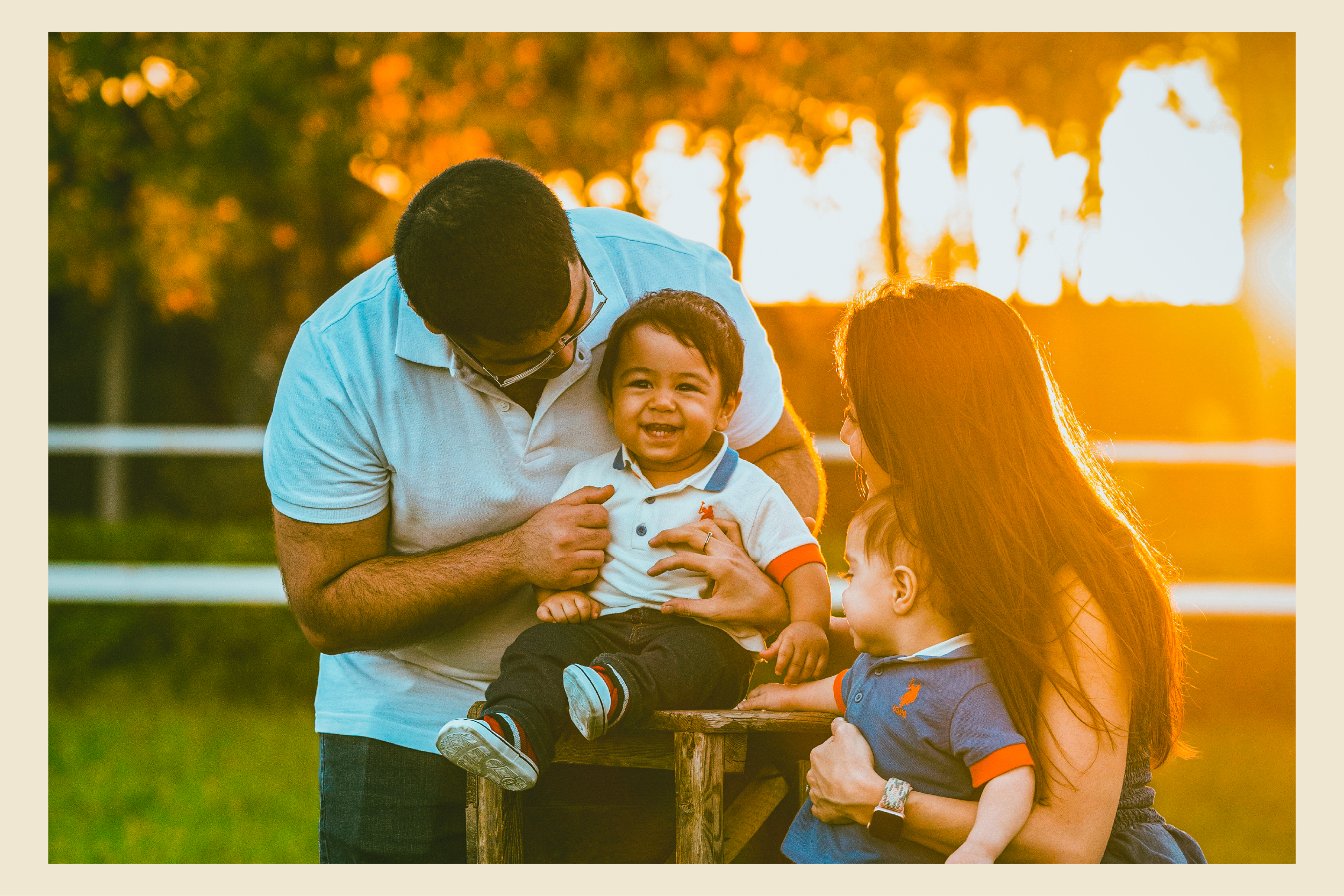 Two parents and two young children sit by a fence at sunset.
