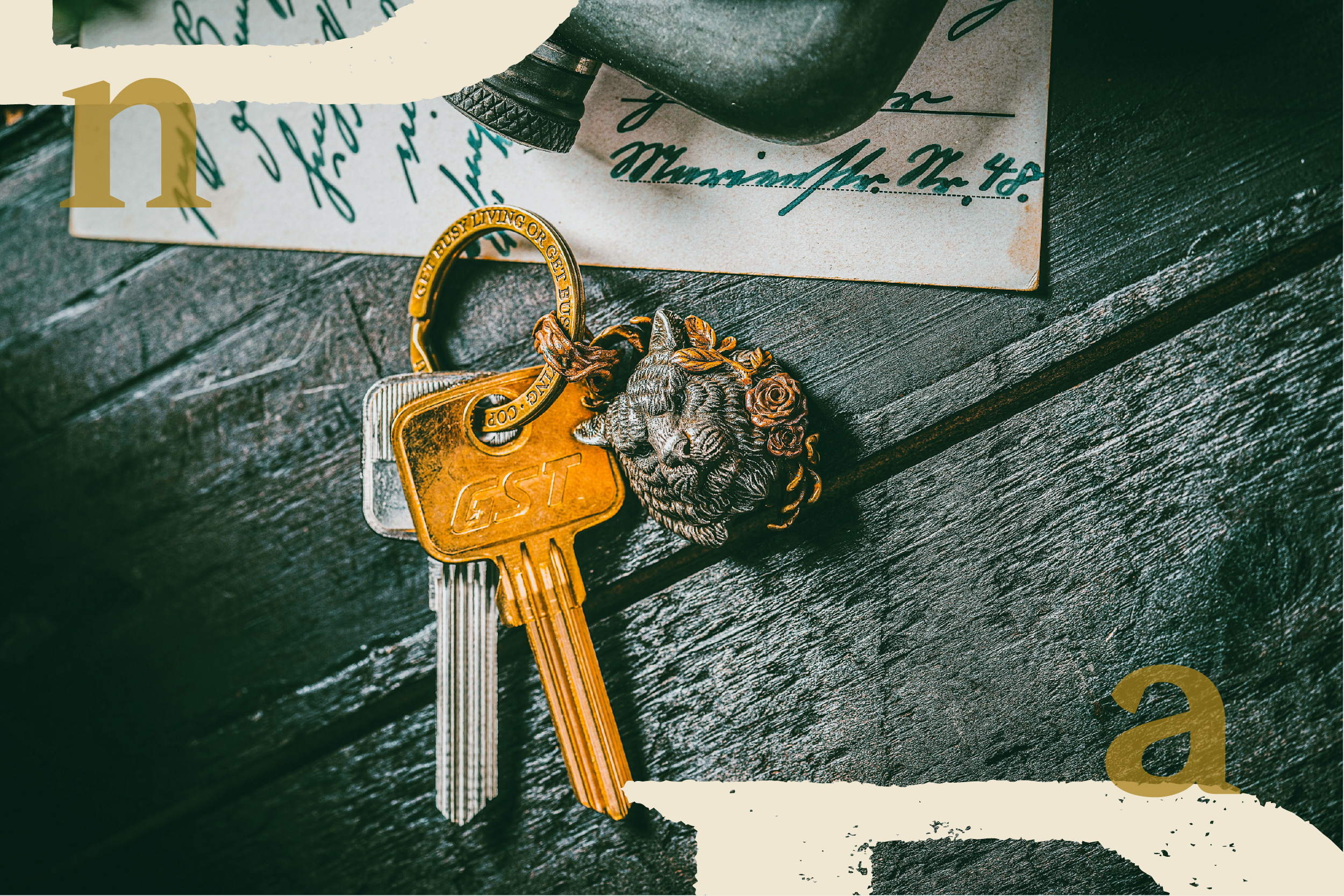Brass keys with a lion-head keyring rest on dark wood near old letters.