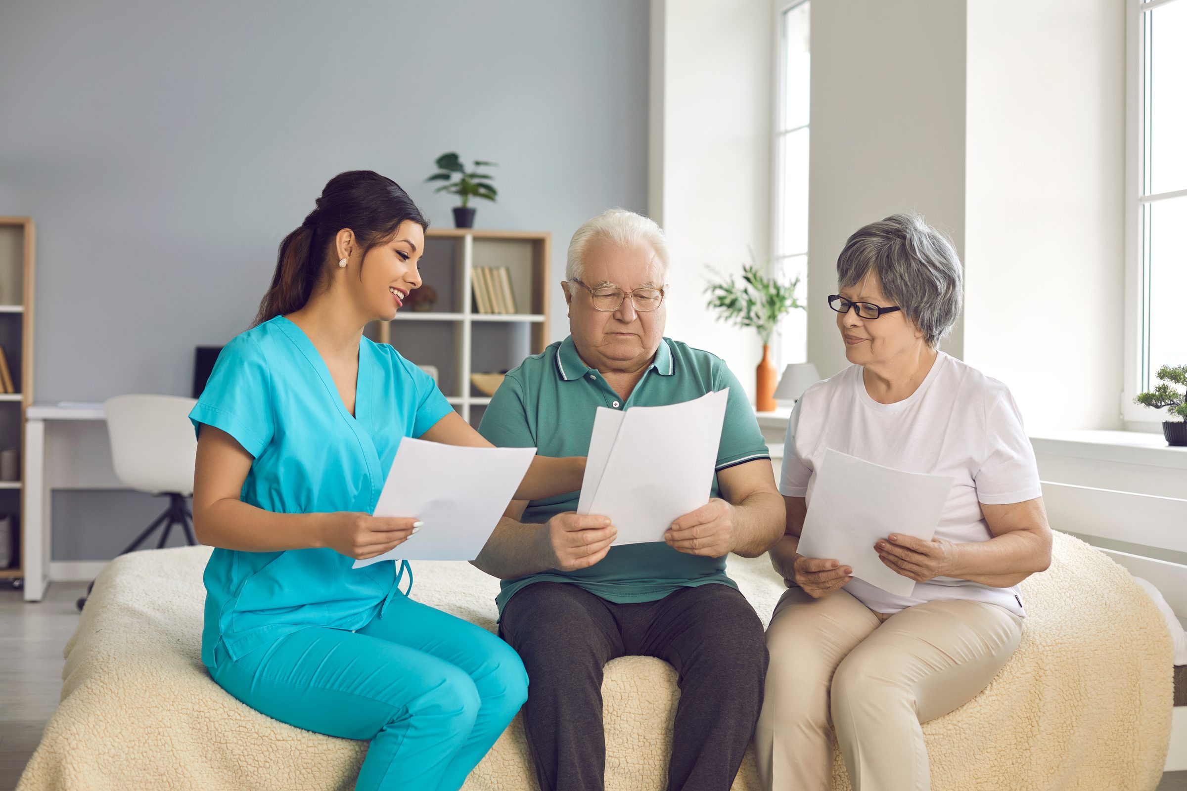 A home health nurse reviewing care paperwork with an older couple on their sofa