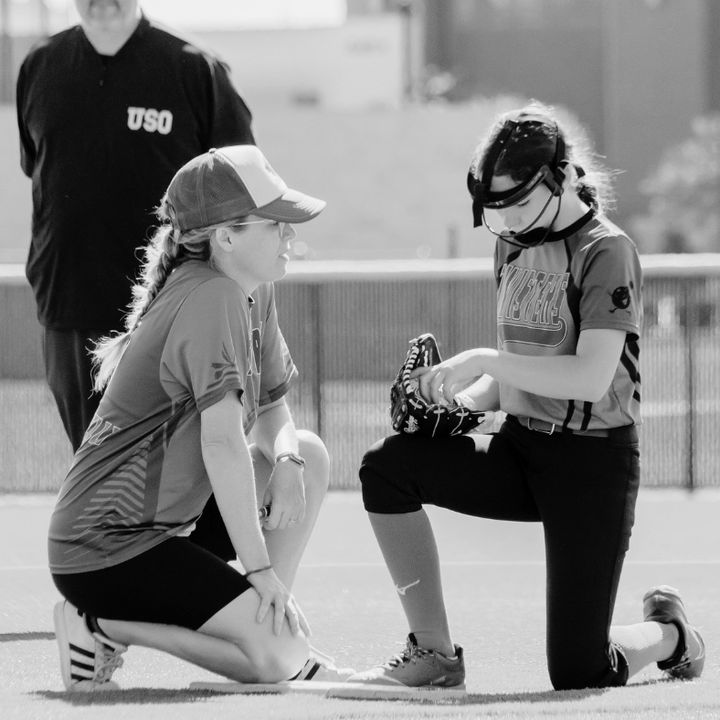 A coach kneeling on the infield working with a young pitcher
