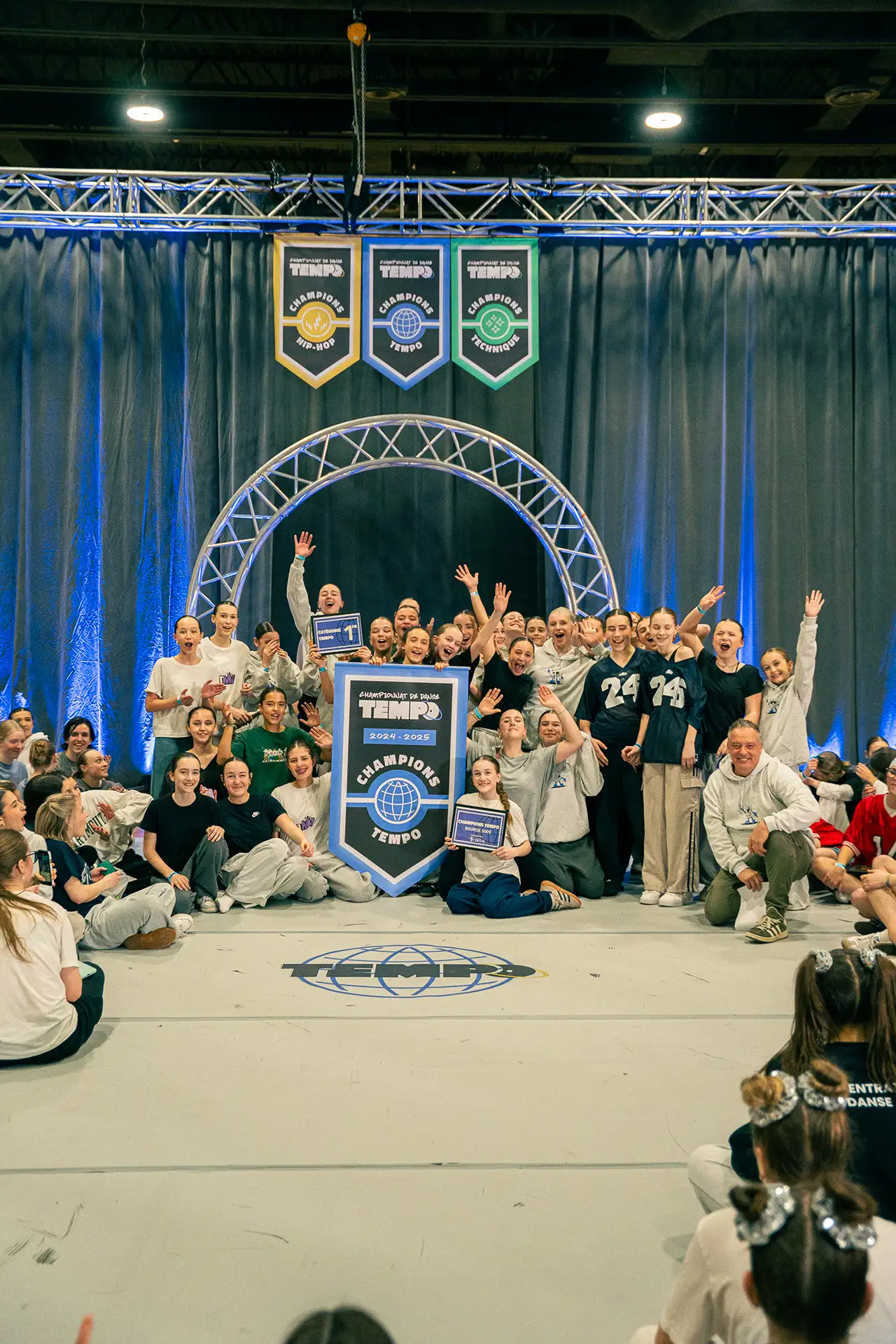 Les animateurs s'adressent aux danseurs assis autour du plancher, au Championnat Tempo 2025