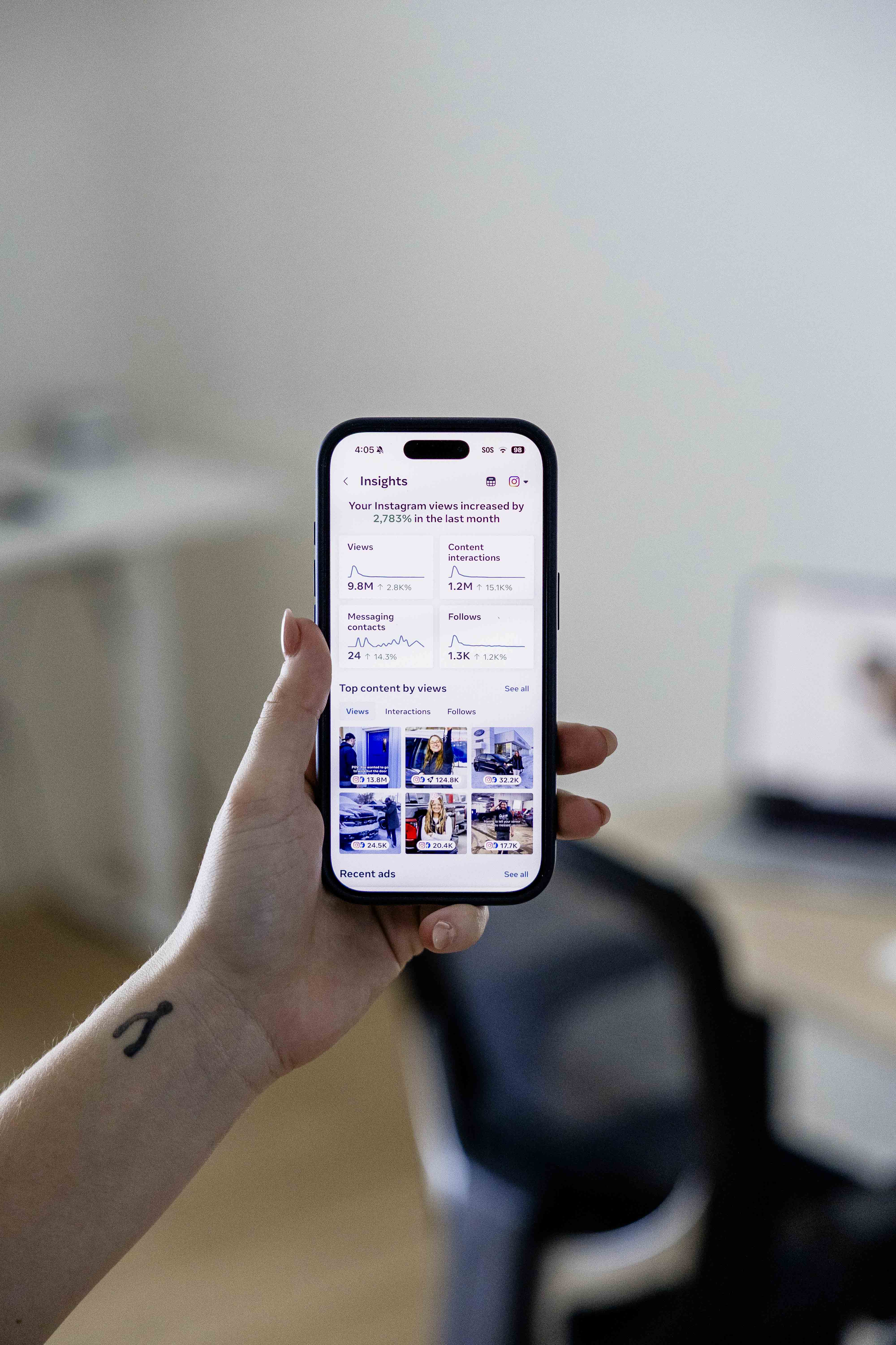 Hand holding a smartphone showing Instagram Insights with view counts and follower growth