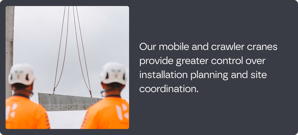 Two workers in orange safety gear and white helmets watching a large concrete beam being lifted by crane cables against a gray sky.