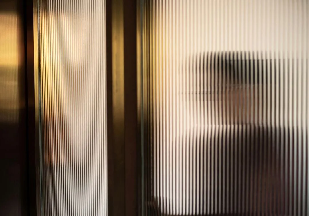 A figure blurred behind fluted glass in warm light