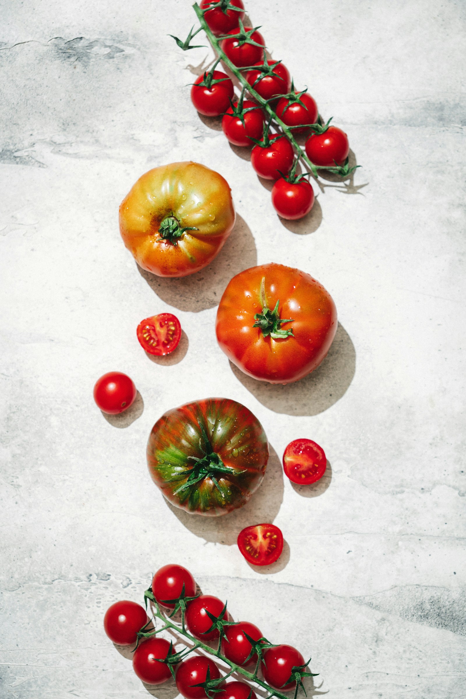 Red, yellow and green-striped tomatoes arranged on a pale surface with cherry tomatoes still on the vine.