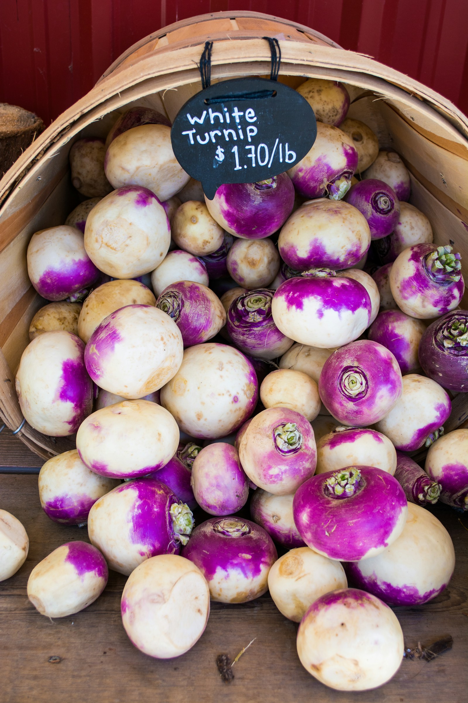 White and purple-topped turnips piled in a basket beneath a handwritten market sign.