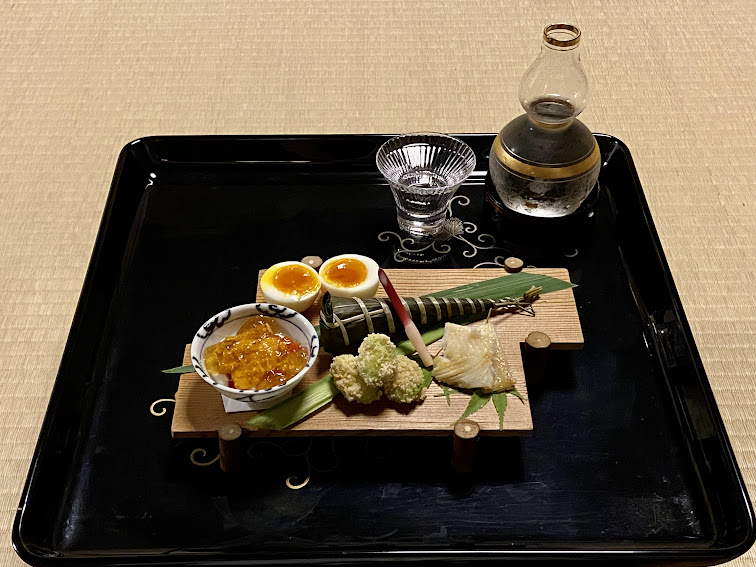 A lacquer tray at Hyōtei holding soft-boiled egg halves, several small preparations, a sake vessel and a glass.