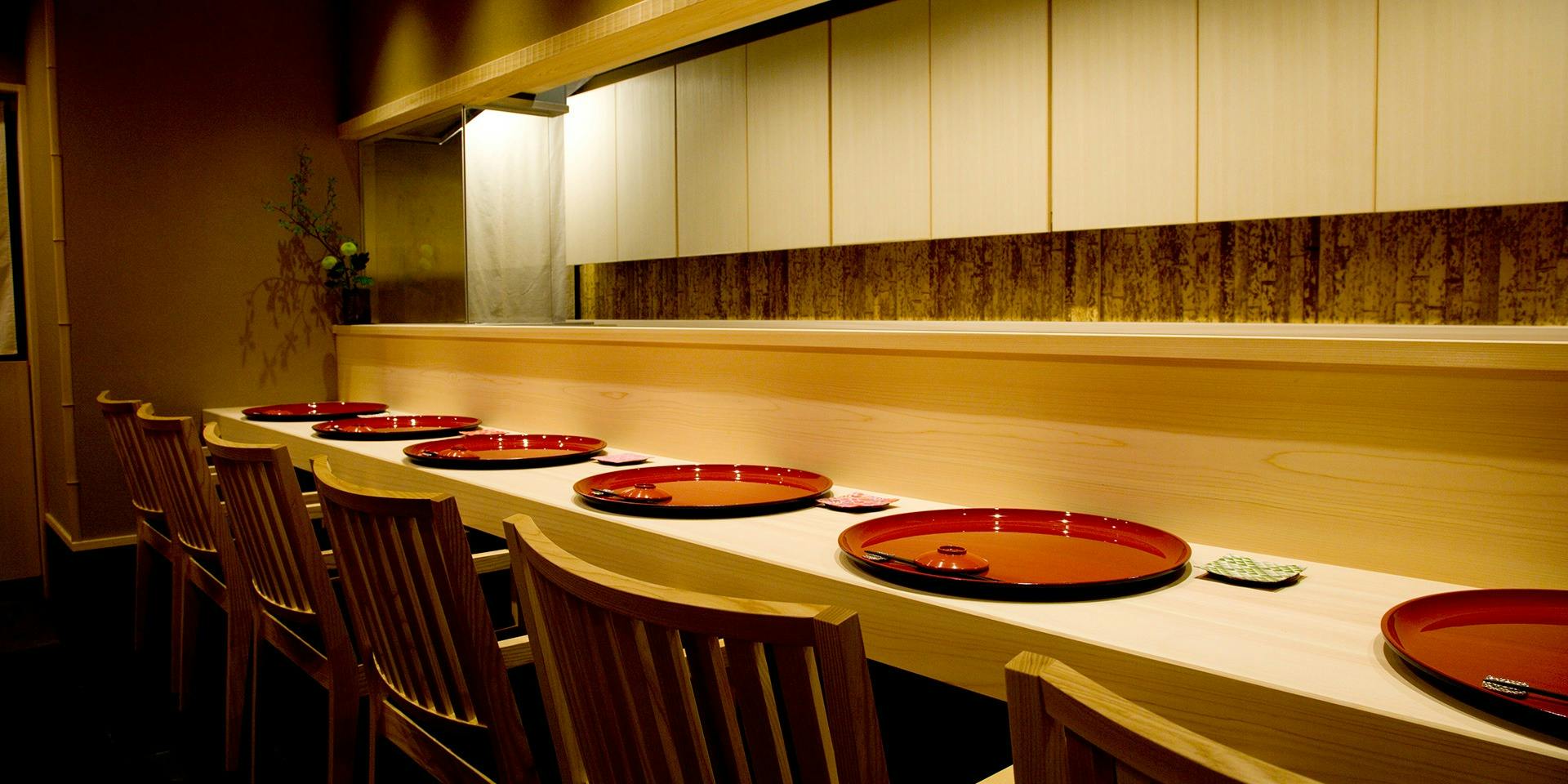 Gion Hanamai’s pale wooden dining counter, set with red lacquer trays and six chairs.