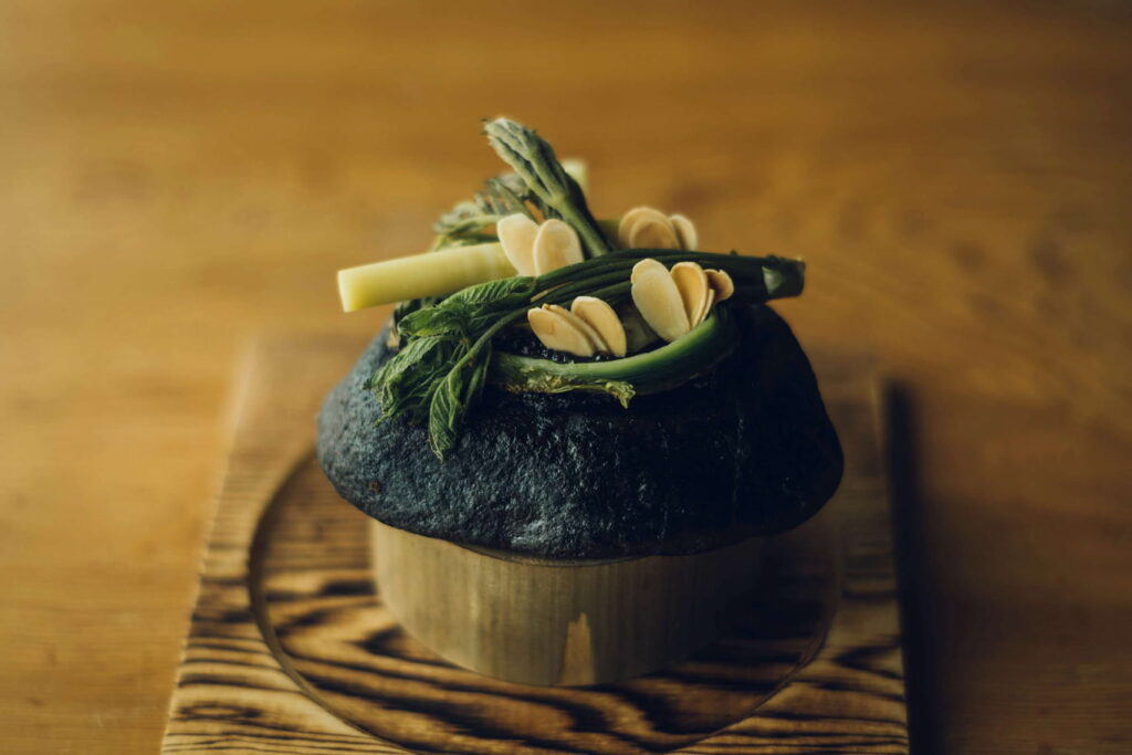 Greens and other plant ingredients arranged on a dark serving surface at Miyamasou.