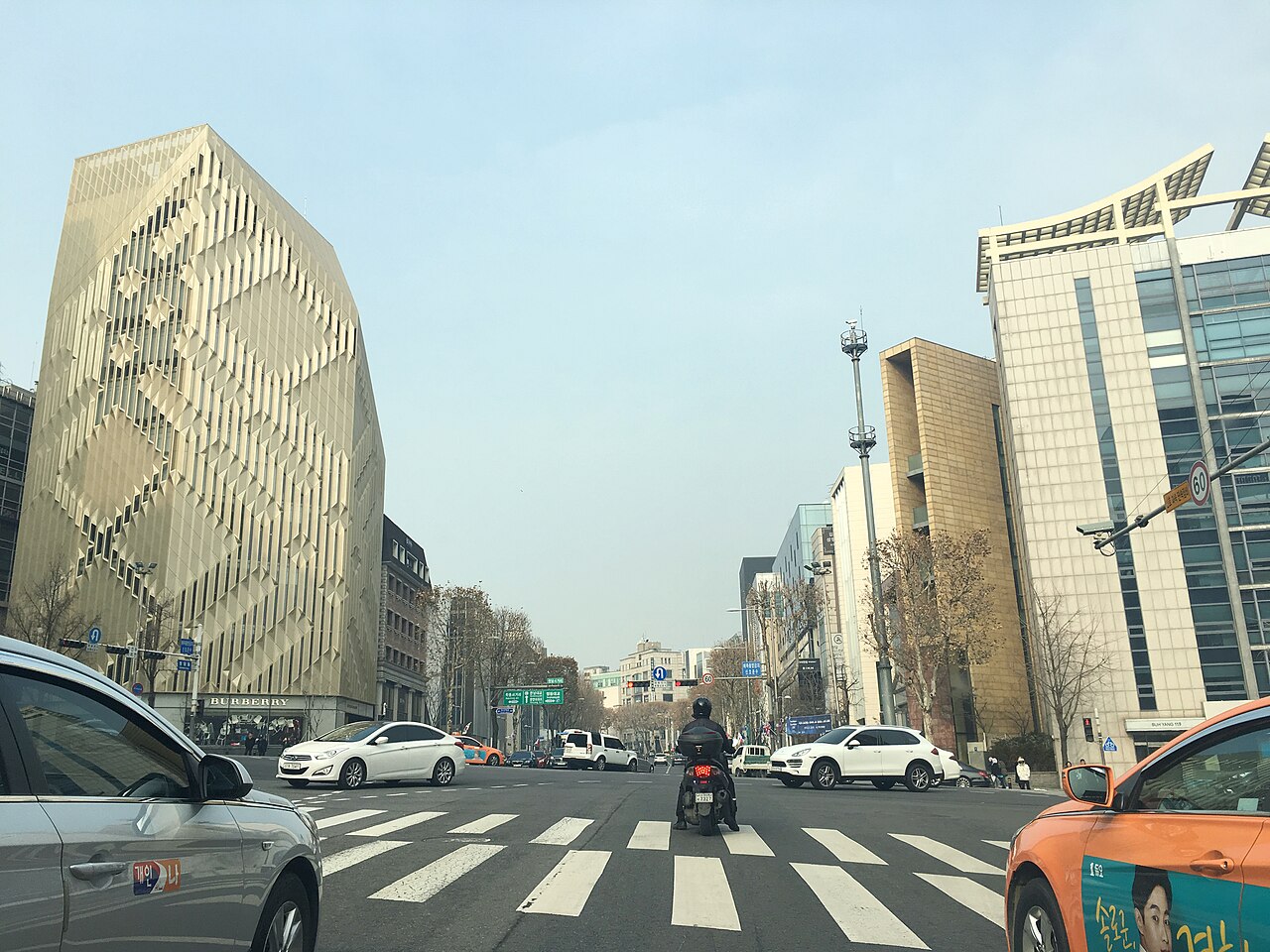 Traffic and pedestrians at Cheongdam Intersection, with a gold-toned Burberry building on the corner.