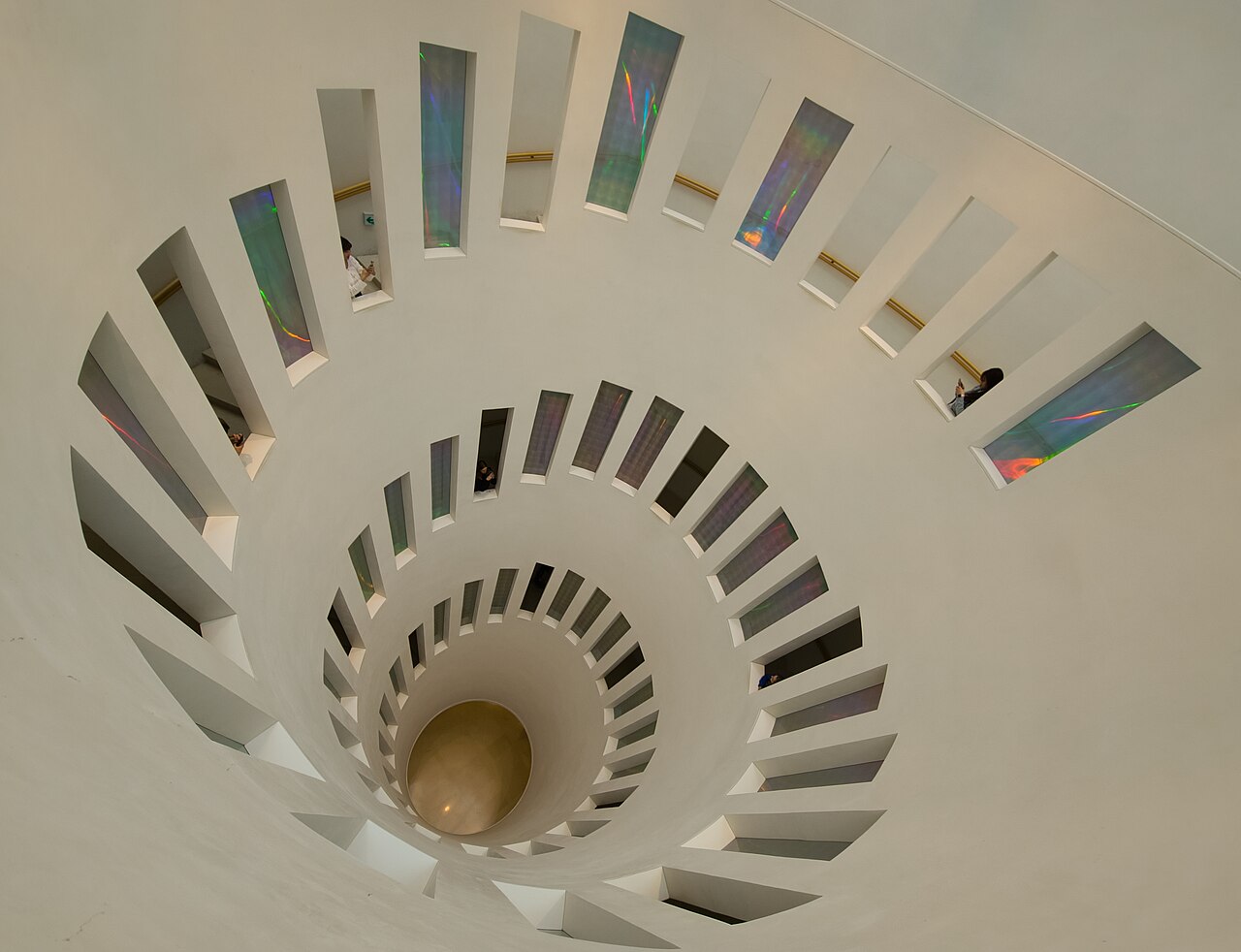 A downward view through Leeum’s curved staircase, showing pale walls, repeated openings and coloured glass.