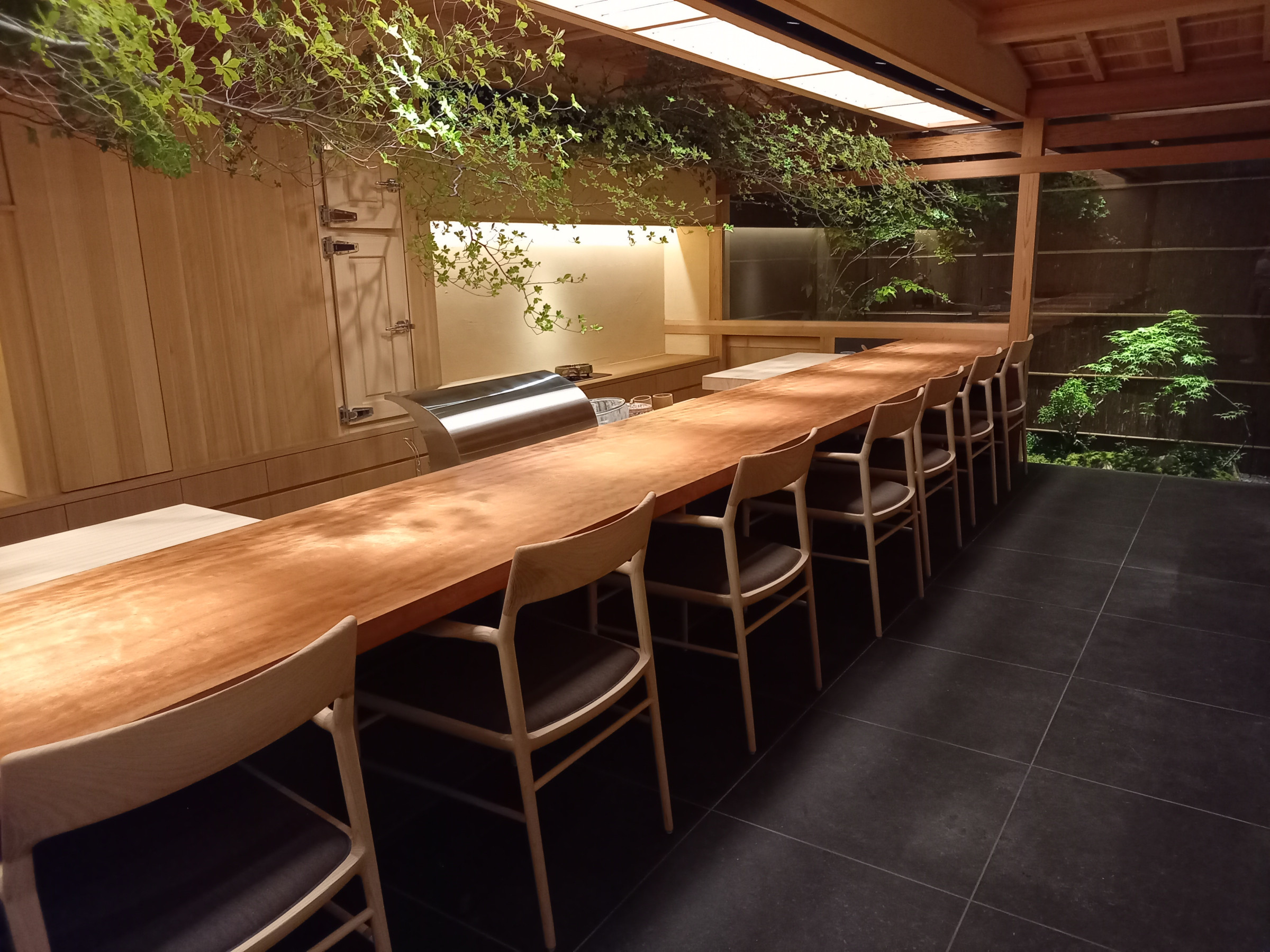 Long straight wooden counter with backed chairs and a partly screened frying station at Tempura Motoyoshi in Ebisu.