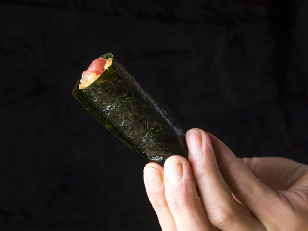Close view of a small nori hand roll with tuna and seasoned rice at Hakkoku.