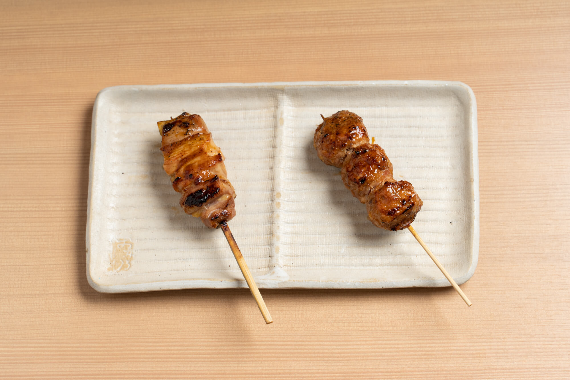 Chicken thigh and tsukune skewers served on a rectangular plate at Yakitori Omino.