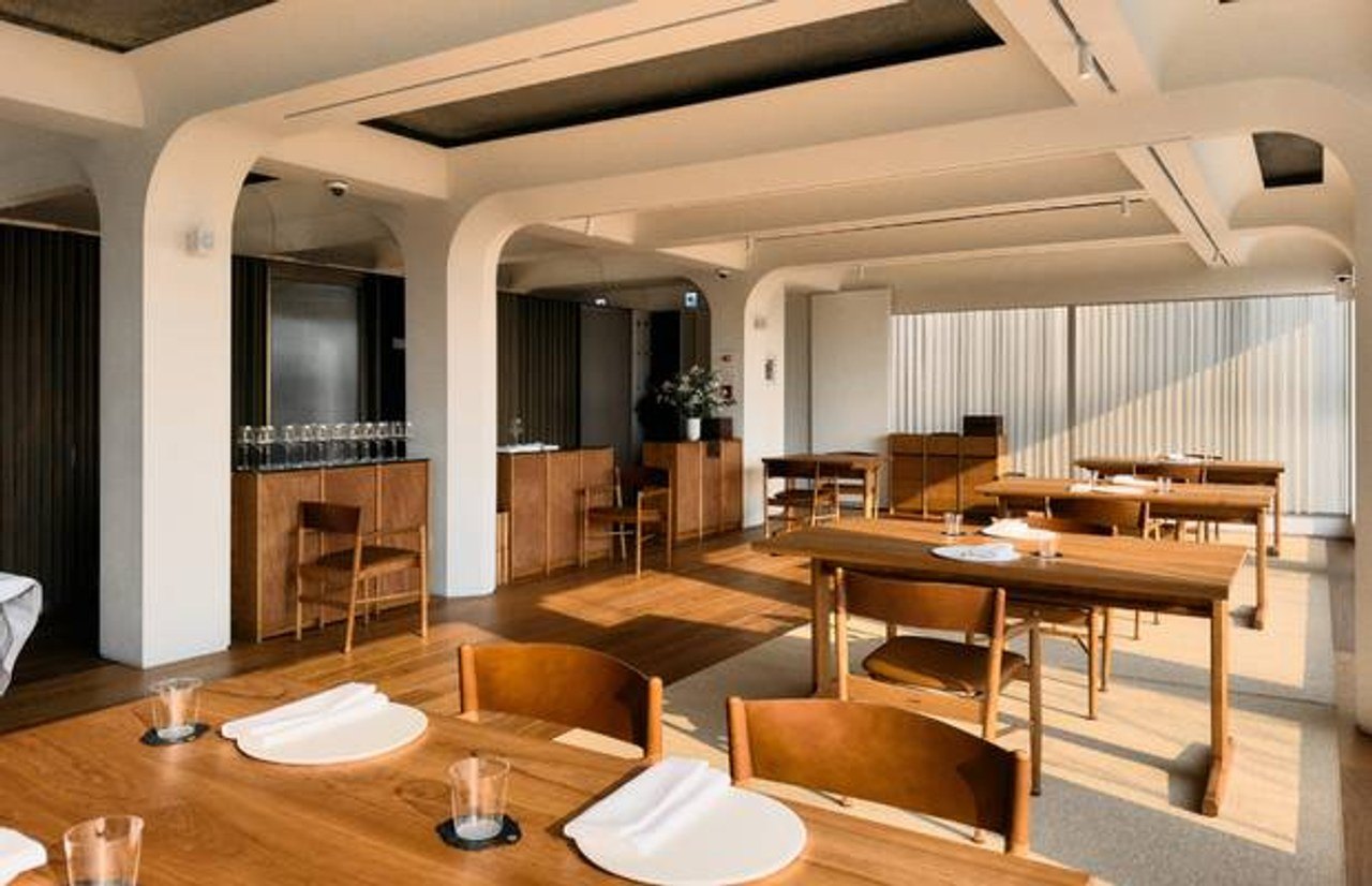 Mosu dining room with warm wood tables, windows and curved white structural details.