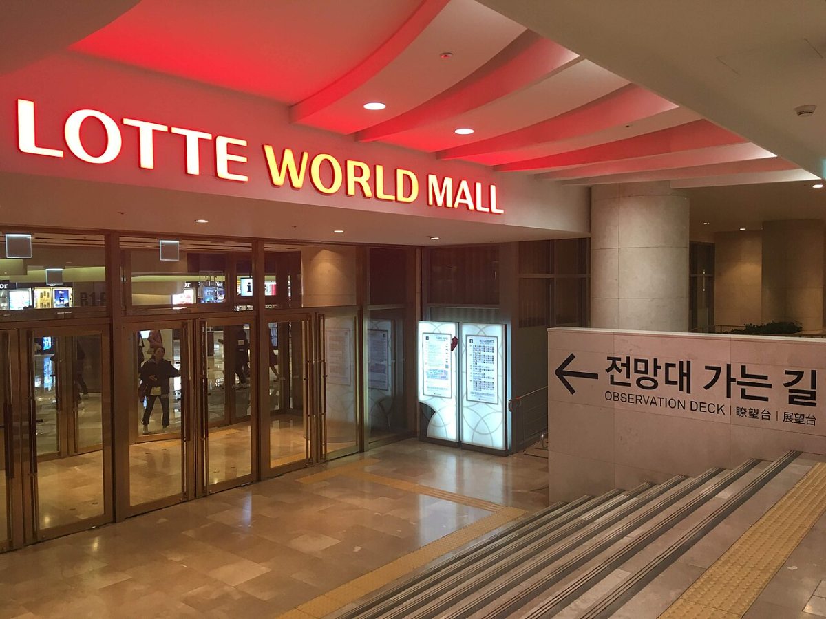 A street entrance to Lotte World Mall in 2018, with glass doors and signage for the adjoining complex.