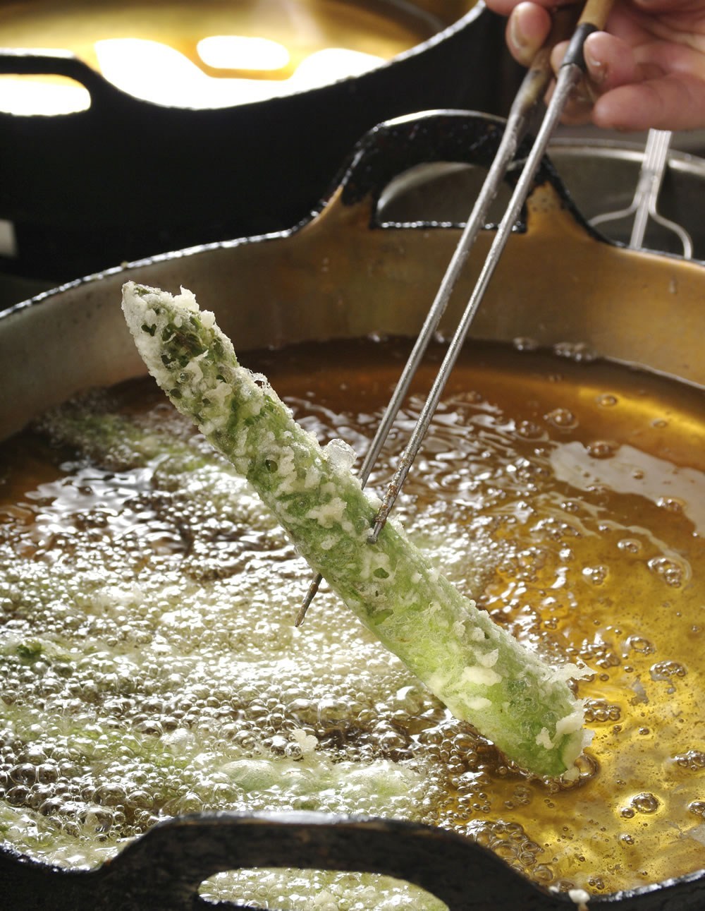 An asparagus spear being lifted above a tempura frying pan at Tempura Kondo.