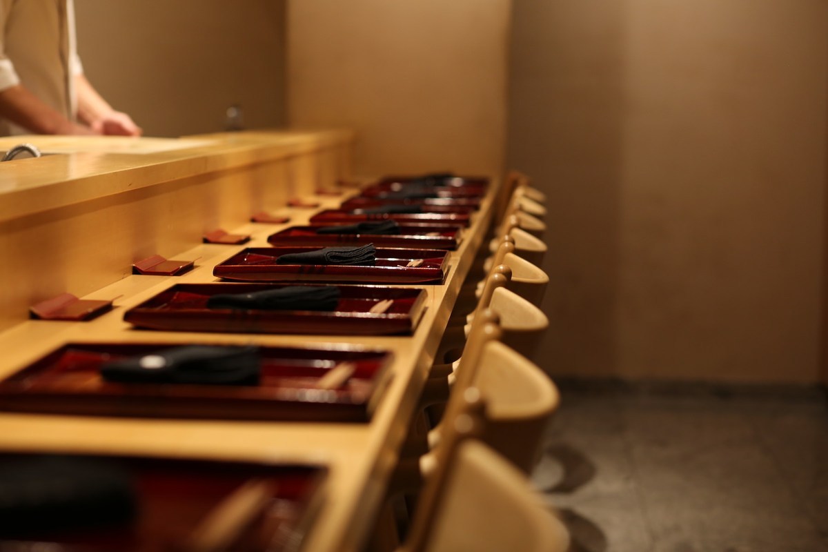 An angled view along Ginza Shinohara’s wooden dining counter towards the working area behind it.