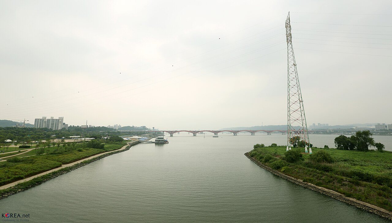 The Han River beside Seonyudo, with a riverside path and the arched pedestrian bridge visible in the distance.