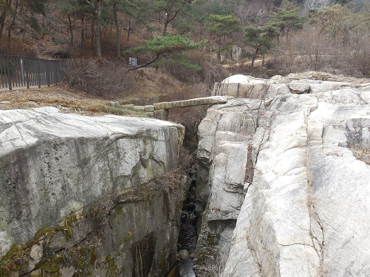 Giringyo’s narrow stone span among exposed granite in Suseongdong Valley, with a public path beside the rocks, photographed in March 2020.