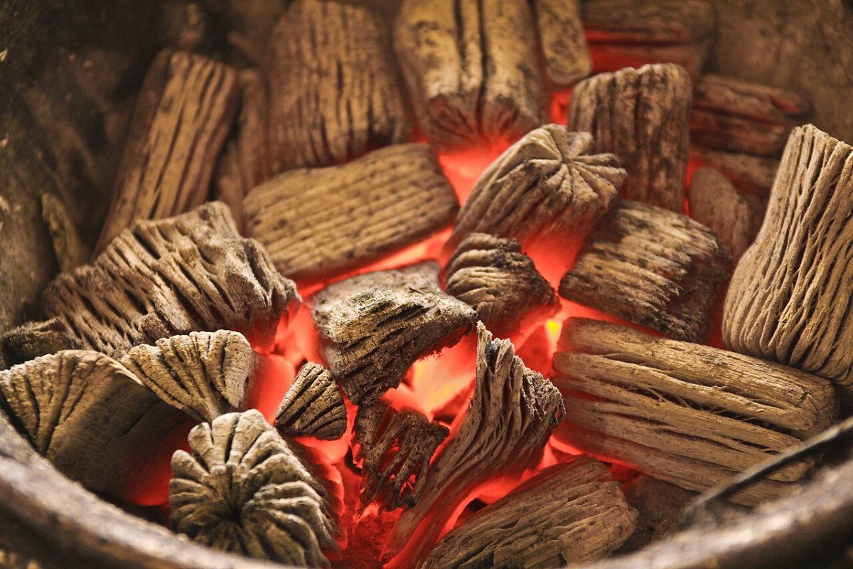 Close view of glowing charcoal embers beneath dark, cracked wood surfaces.