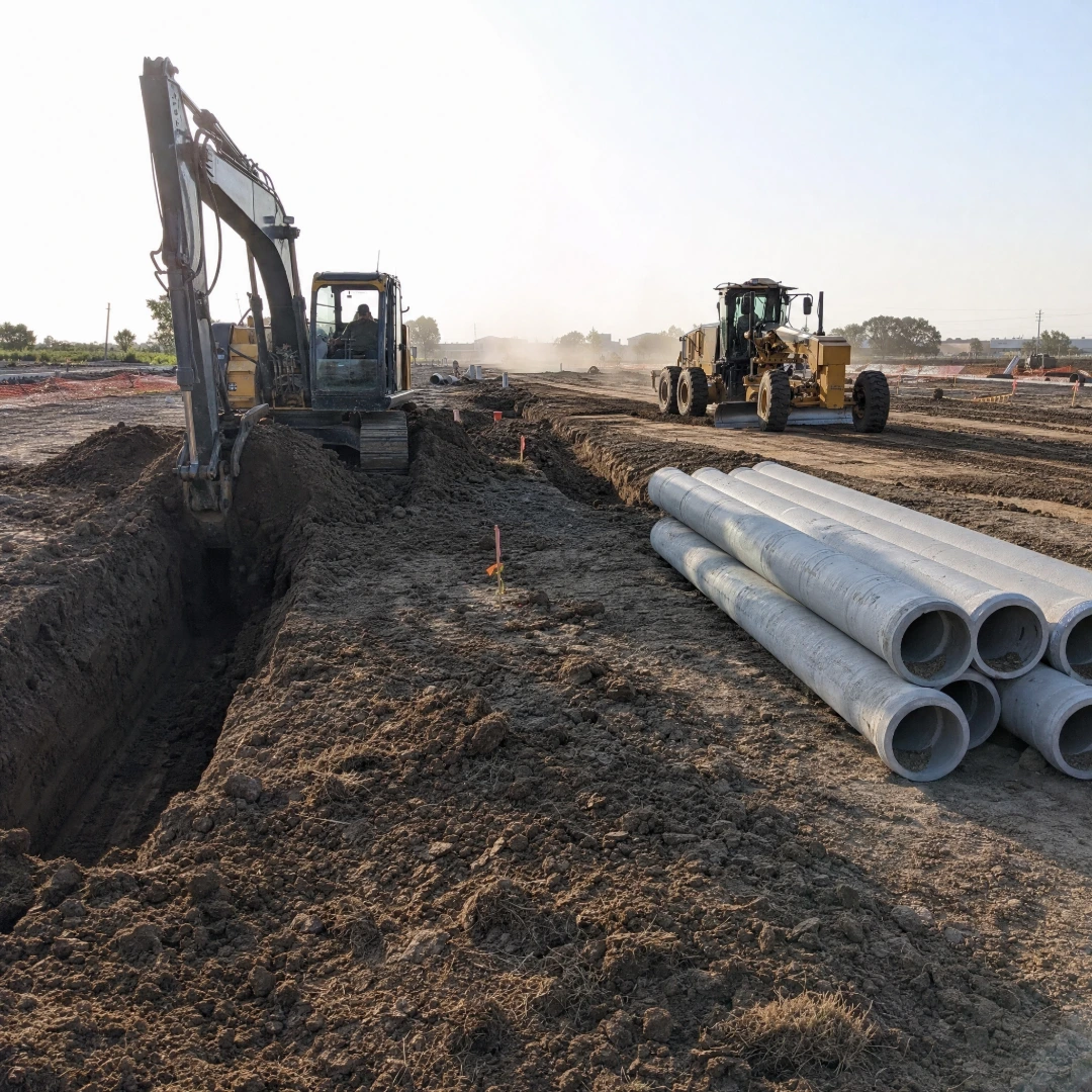 Excavator and dozer moving dark clay soil during site work and grading ahead of commercial construction