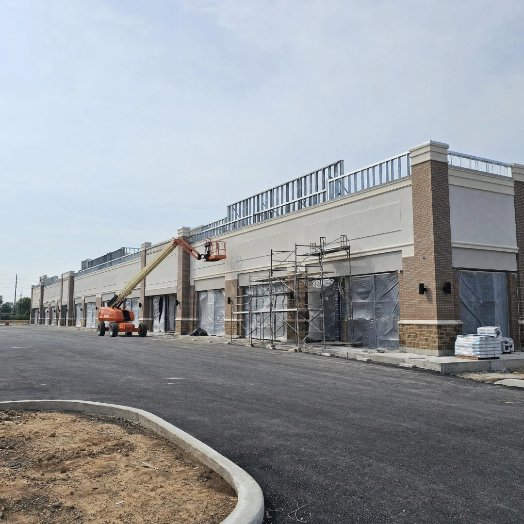 Retail strip center under construction with framed storefront bays, a stucco facade and a new parking lot