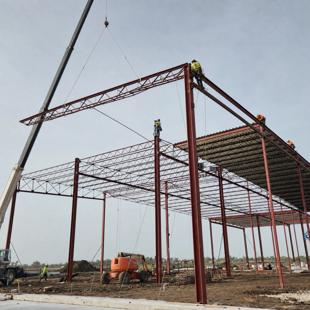 Structural steel frame of a commercial building with bolted beams and columns rising against a bright sky