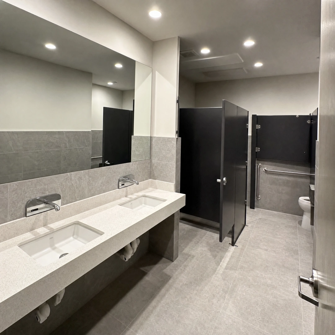 Renovated commercial restroom with an ADA-accessible stall, grab bars, floor-mounted partitions and a wall-hung sink