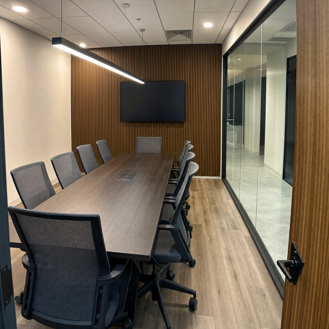 Renovated conference room with a long wood table, upholstered chairs, a wall-mounted display and new carpet tile