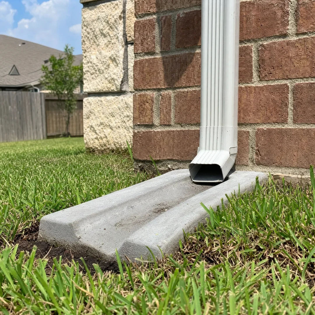 Downspout elbow discharging onto a concrete splash block to carry roof runoff away from the foundation