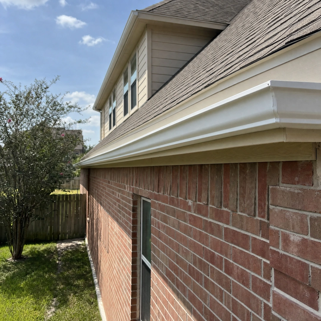 Newly installed white 6-inch K-style seamless aluminum gutter running along the roofline of a two-story red brick home