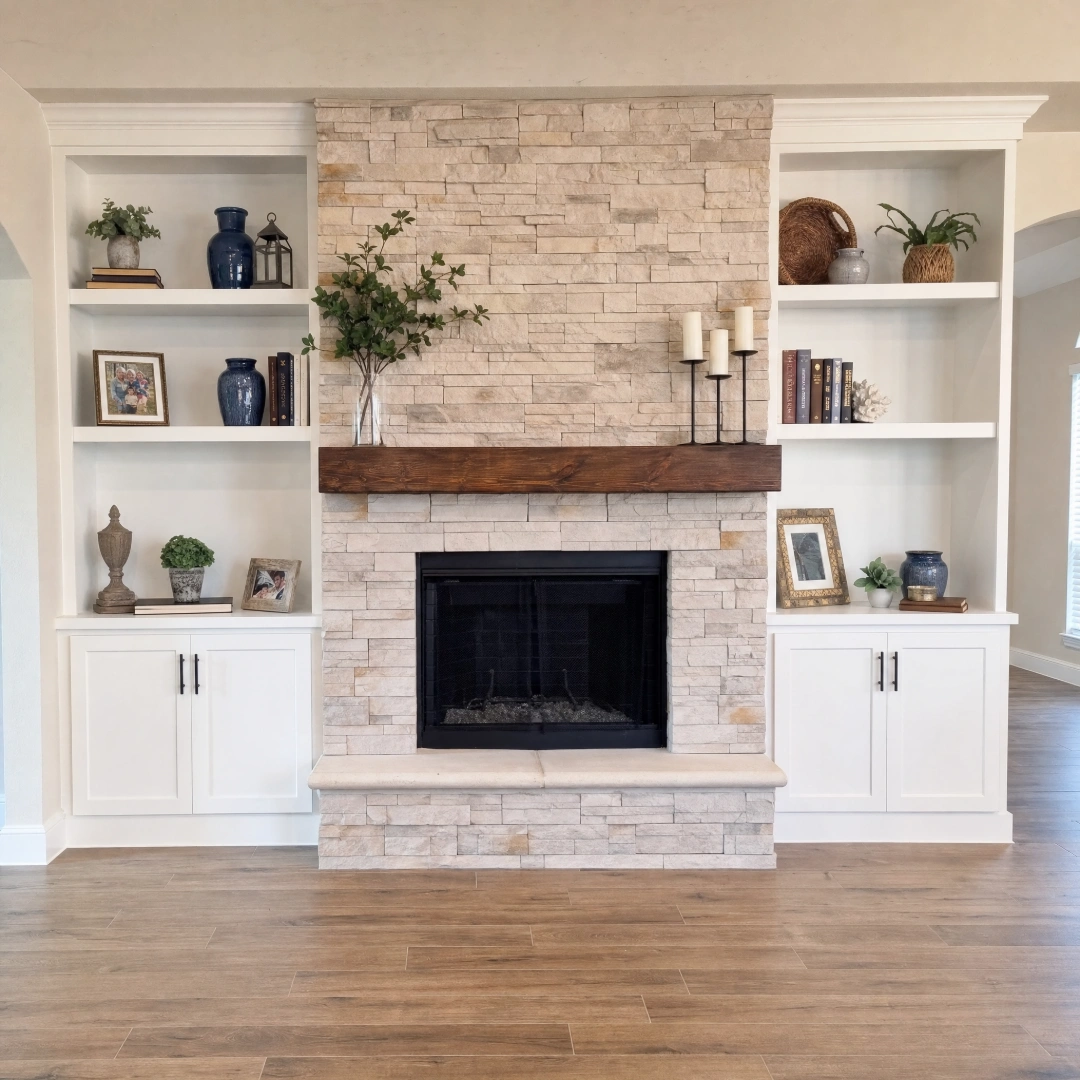 Stacked stone fireplace with a wood mantel flanked by floor-to-ceiling white built-in cabinetry and open shelving