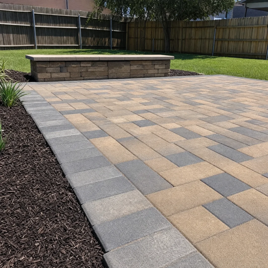Paver patio and stone hardscape laid across a backyard with a border course and landscape beds