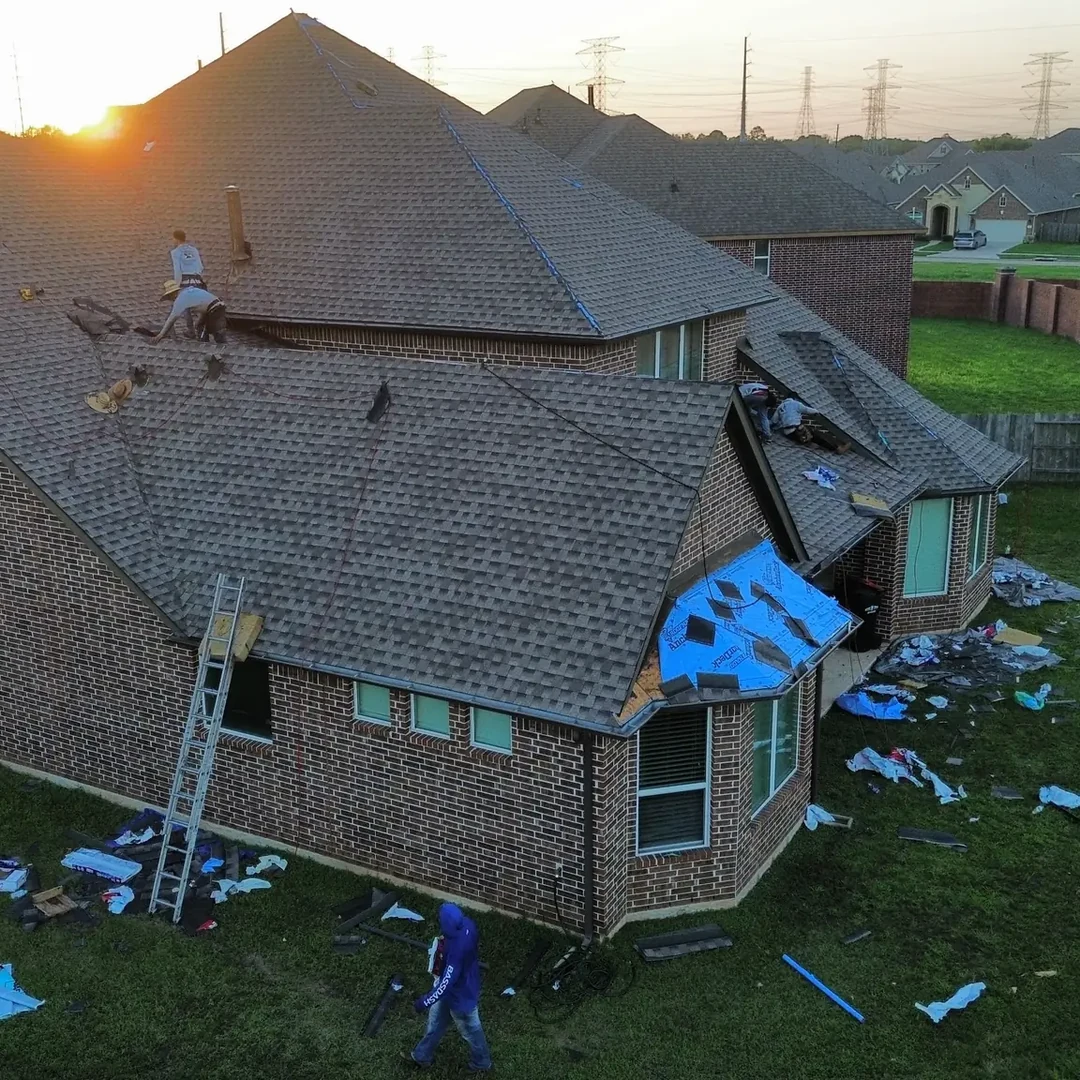 Aerial view at sunrise of a roof replacement in progress on a two-story brick home, with the crew working on the exposed deck