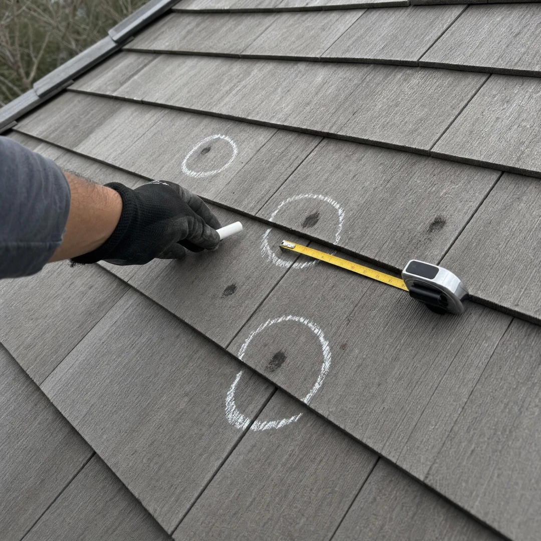 Roof inspection with hail impact points circled in chalk across architectural asphalt shingles