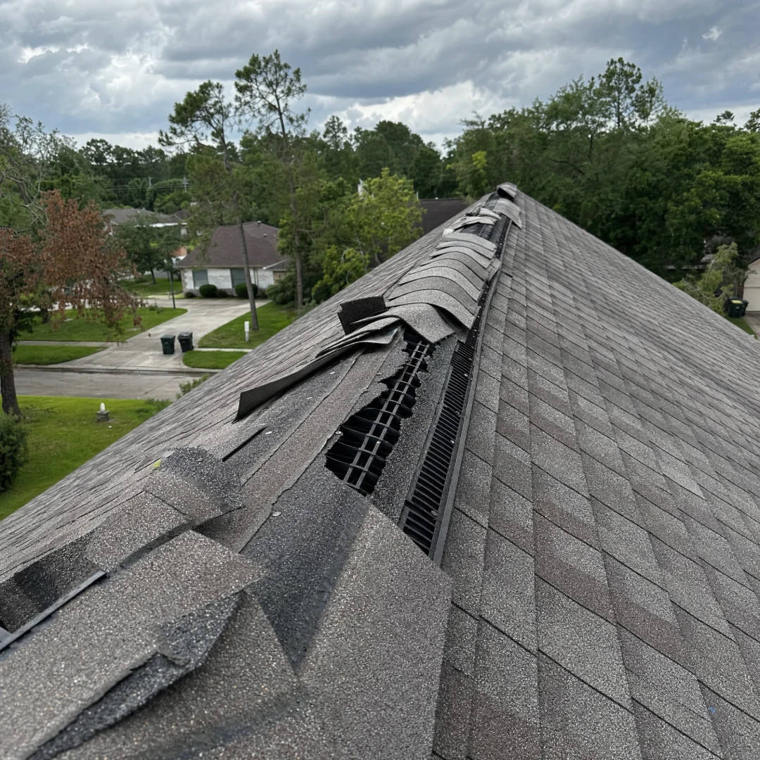 Ridge cap shingles torn loose along the peak of a roof by high wind